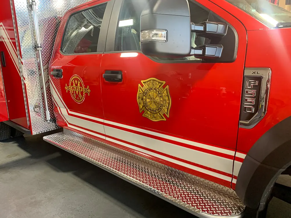 Exterior view of small fire truck showing cab, body compartments, and wheel/tire area.