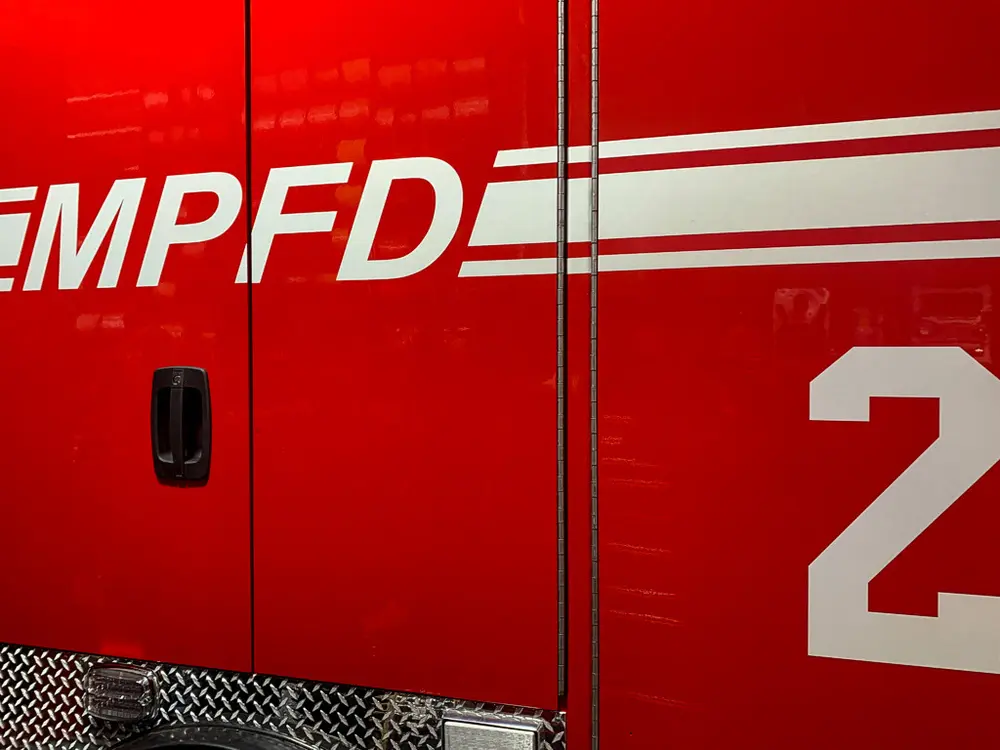 Exterior view of small fire truck showing cab, body compartments, and wheel/tire area.