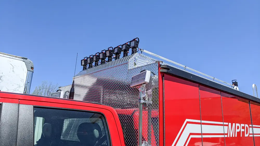 Exterior view of small fire truck showing cab, body compartments, and wheel/tire area.