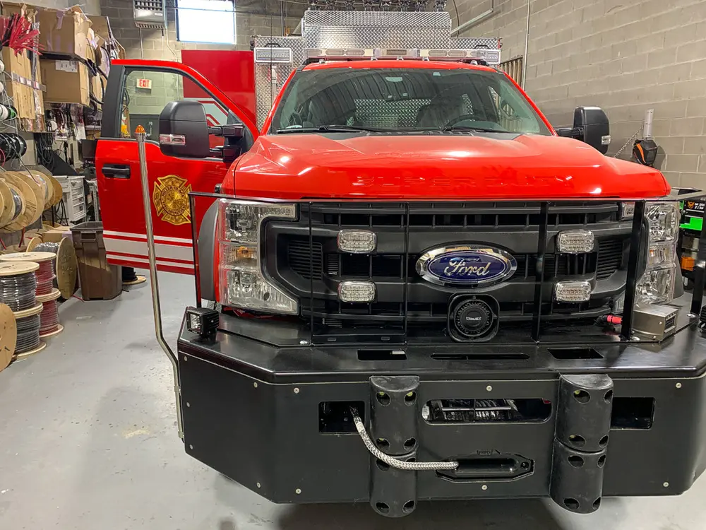 Exterior view of small fire truck showing cab, body compartments, and wheel/tire area.