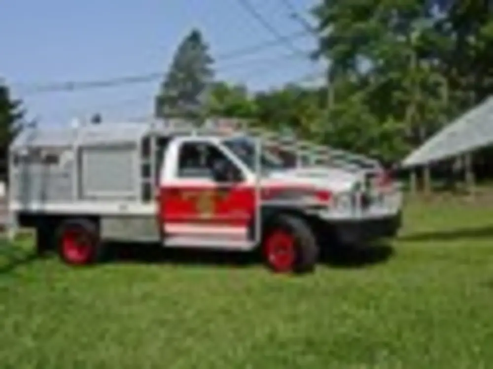 Exterior view of small fire truck showing cab, body compartments, and wheel/tire area.