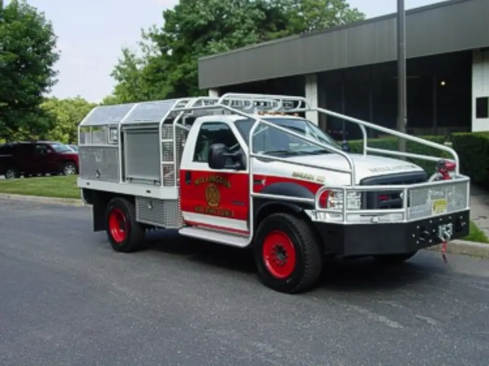 Exterior view of small fire truck showing cab, body compartments, and wheel/tire area.