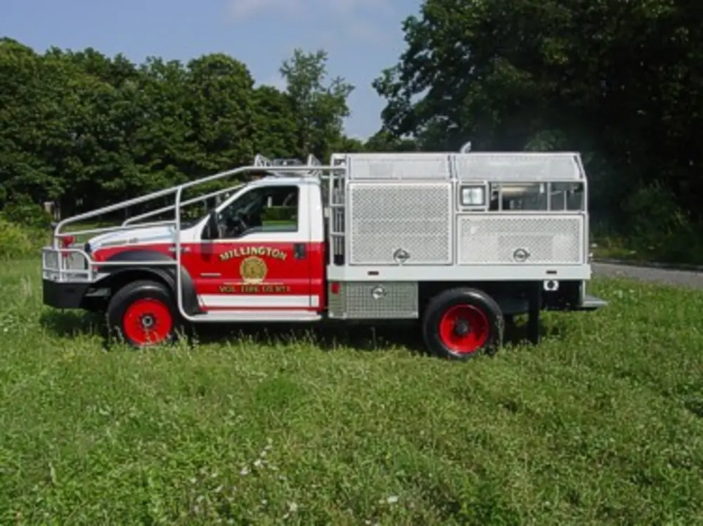 Exterior view of small fire truck showing cab, body compartments, and wheel/tire area.