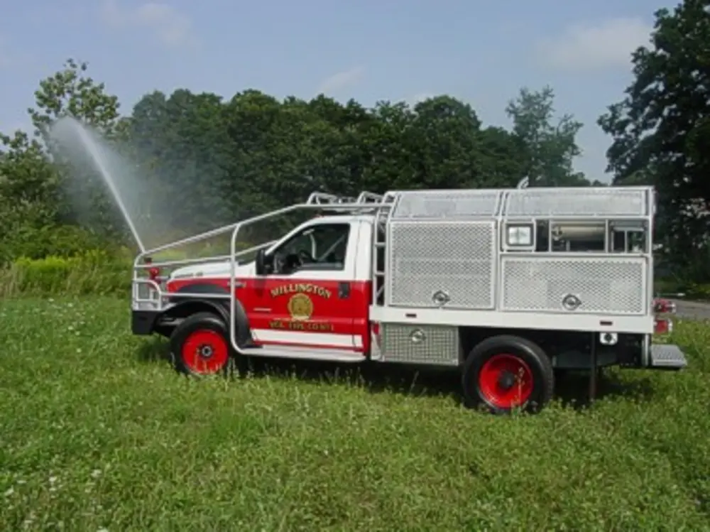 Exterior view of small fire truck showing cab, body compartments, and wheel/tire area.