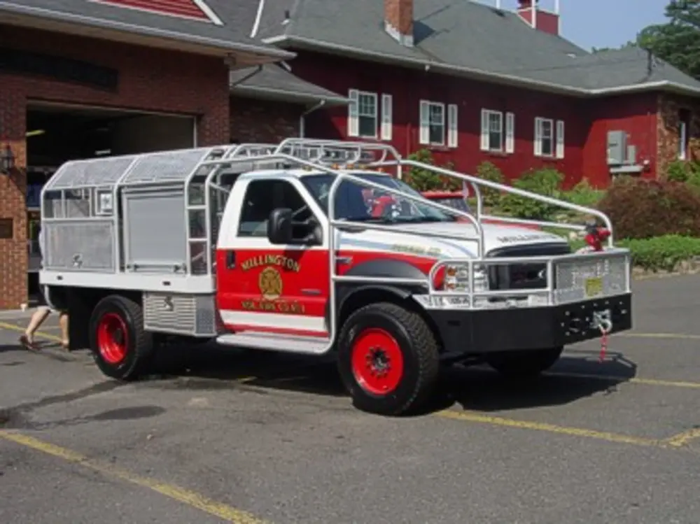 Exterior view of small fire truck showing cab, body compartments, and wheel/tire area.