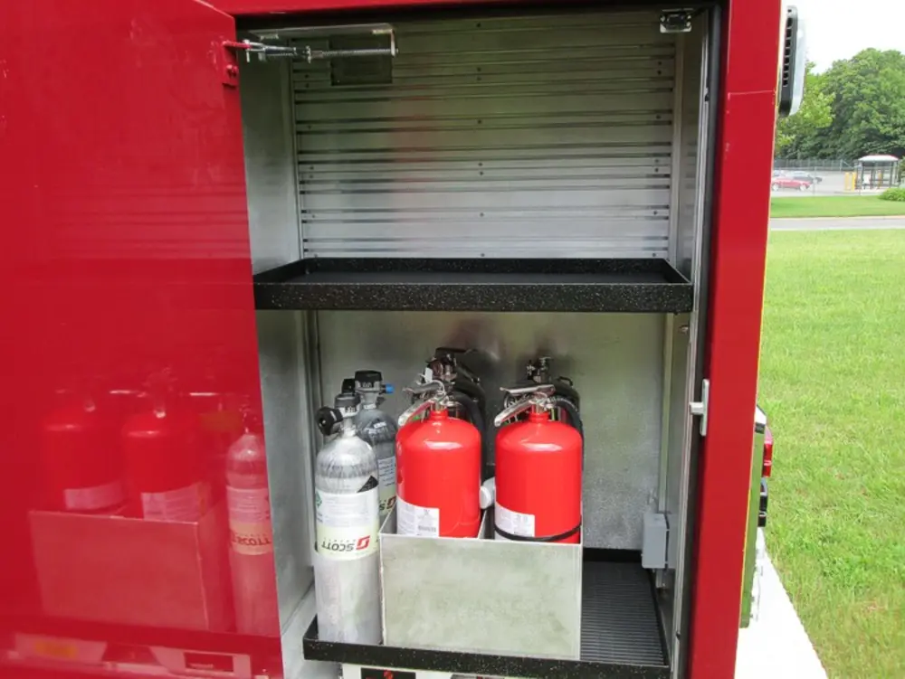 Exterior view of small fire truck showing cab, body compartments, and wheel/tire area.
