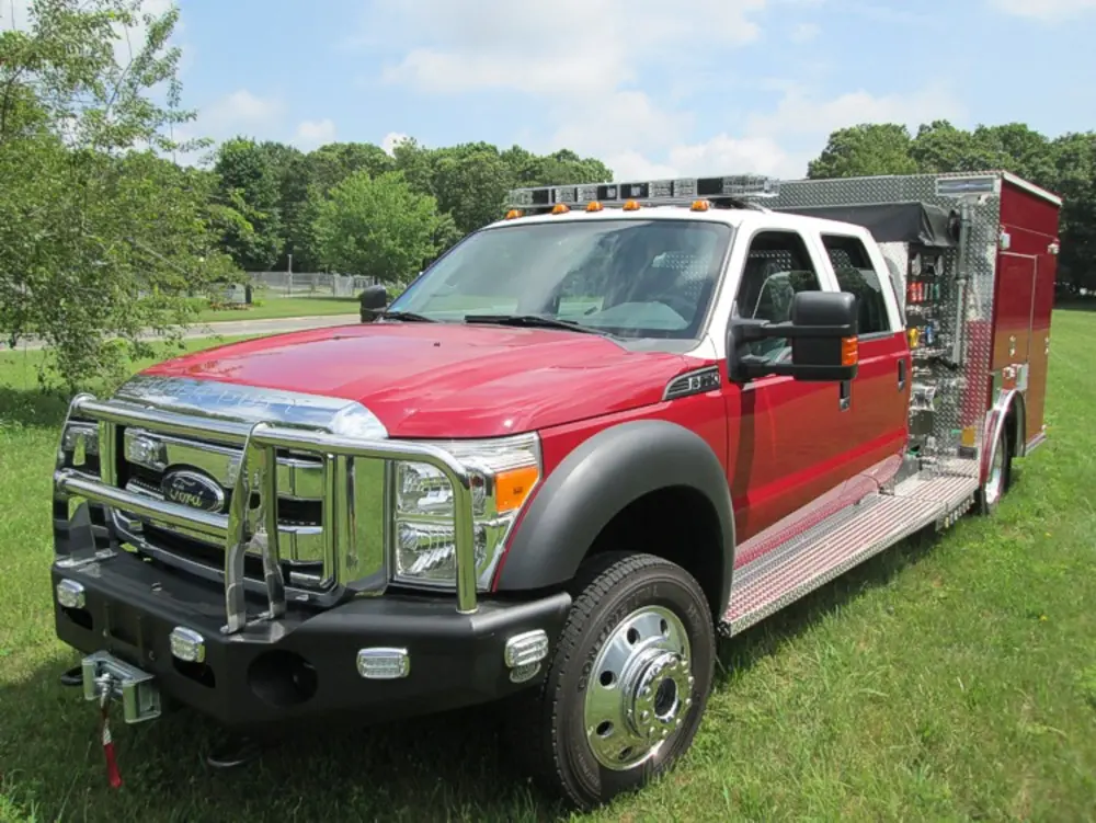 Exterior view of small fire truck showing cab, body compartments, and wheel/tire area.
