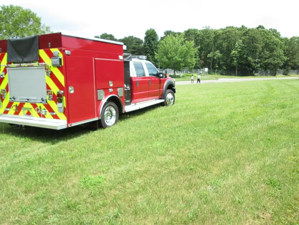 Exterior view of small fire truck showing cab, body compartments, and wheel/tire area.