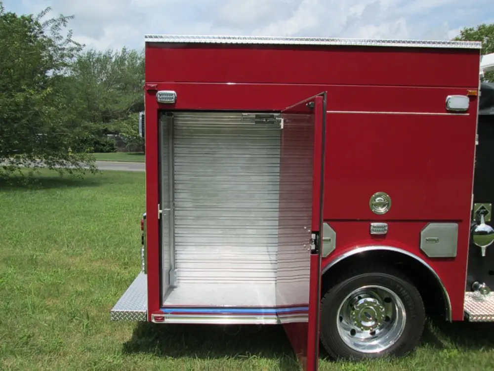 Exterior view of small fire truck showing cab, body compartments, and wheel/tire area.