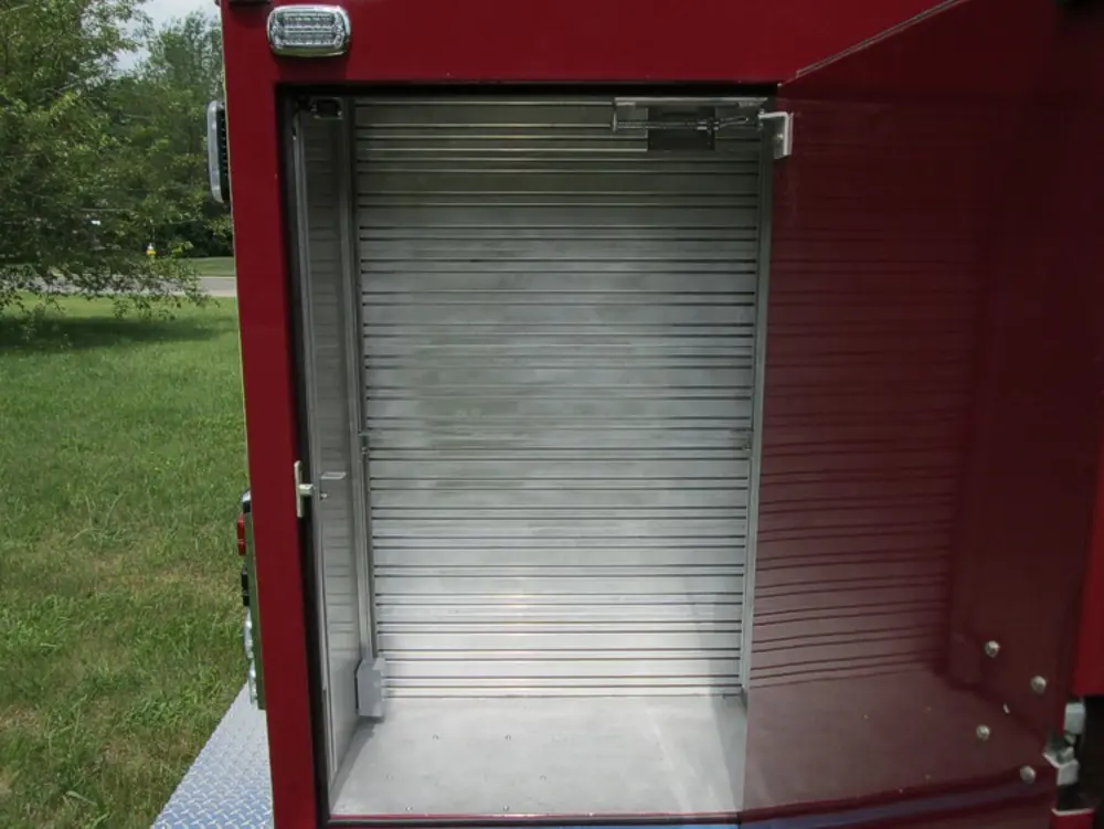 Exterior view of small fire truck showing cab, body compartments, and wheel/tire area.