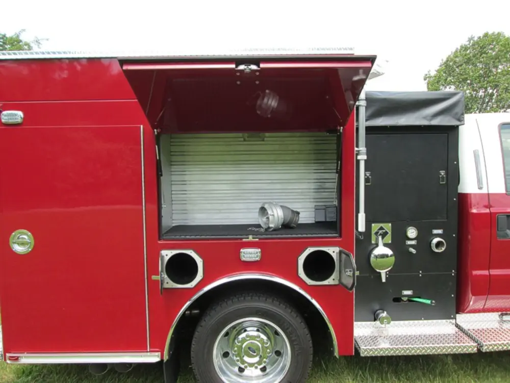 Exterior view of small fire truck showing cab, body compartments, and wheel/tire area.