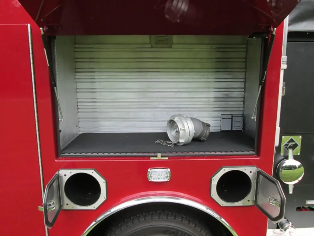 Exterior view of small fire truck showing cab, body compartments, and wheel/tire area.
