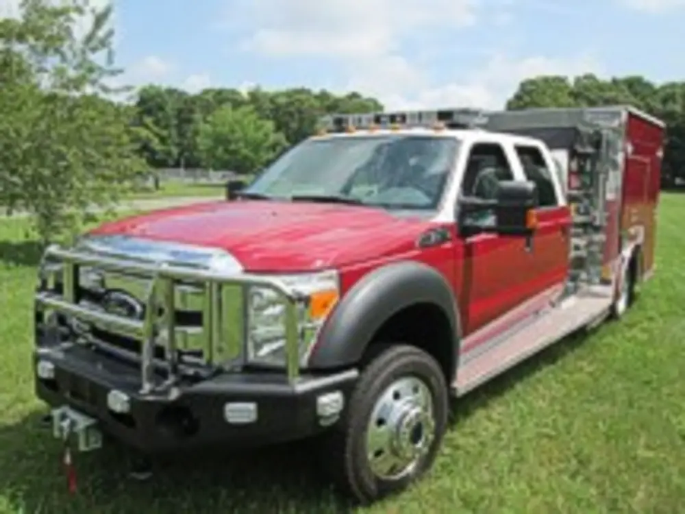 Exterior view of small fire truck showing cab, body compartments, and wheel/tire area.