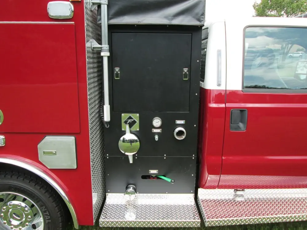 Exterior view of small fire truck showing cab, body compartments, and wheel/tire area.
