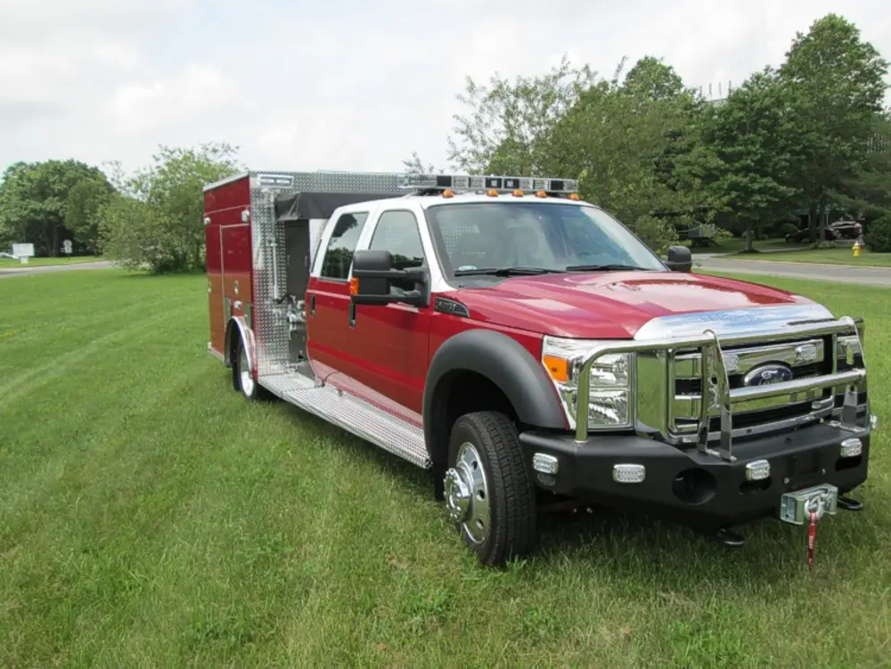 Exterior view of small fire truck showing cab, body compartments, and wheel/tire area.