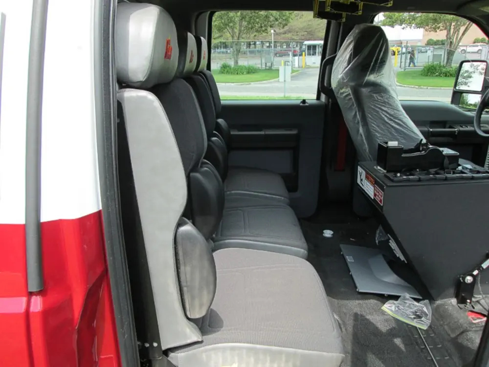 Exterior view of small fire truck showing cab, body compartments, and wheel/tire area.
