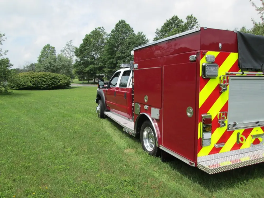 Exterior view of small fire truck showing cab, body compartments, and wheel/tire area.