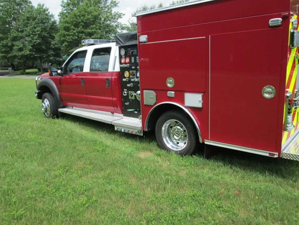 Exterior view of small fire truck showing cab, body compartments, and wheel/tire area.