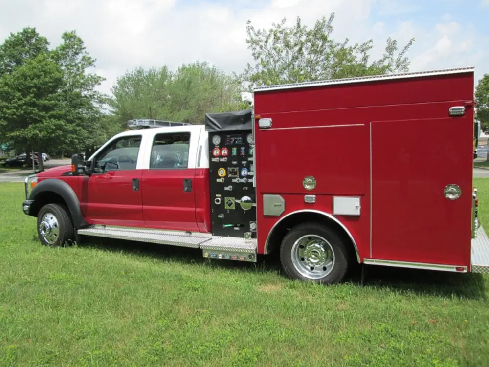 Exterior view of small fire truck showing cab, body compartments, and wheel/tire area.