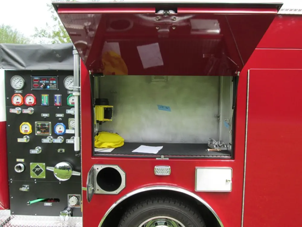 Exterior view of small fire truck showing cab, body compartments, and wheel/tire area.