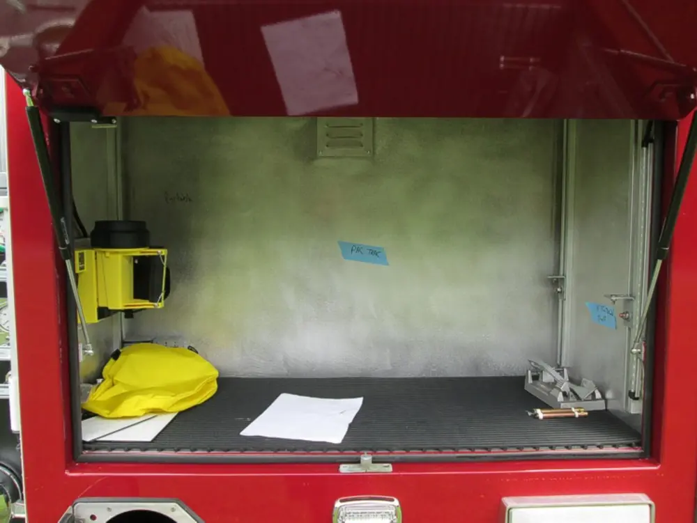 Exterior view of small fire truck showing cab, body compartments, and wheel/tire area.