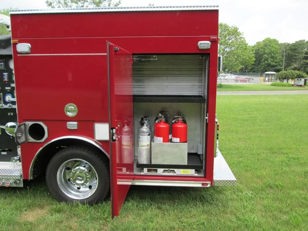 Exterior view of small fire truck showing cab, body compartments, and wheel/tire area.