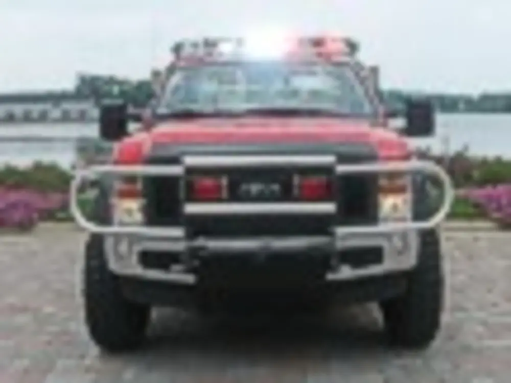 Exterior view of small fire truck showing cab, body compartments, and wheel/tire area.