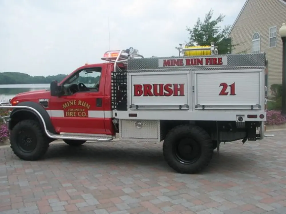 Exterior view of small fire truck showing cab, body compartments, and wheel/tire area.