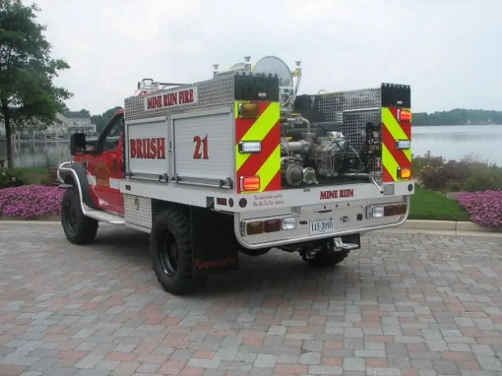 Exterior view of small fire truck showing cab, body compartments, and wheel/tire area.