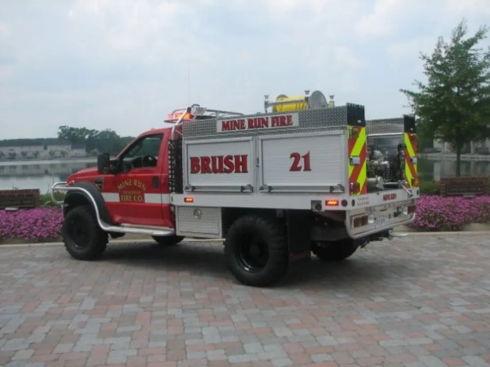 Exterior view of small fire truck showing cab, body compartments, and wheel/tire area.