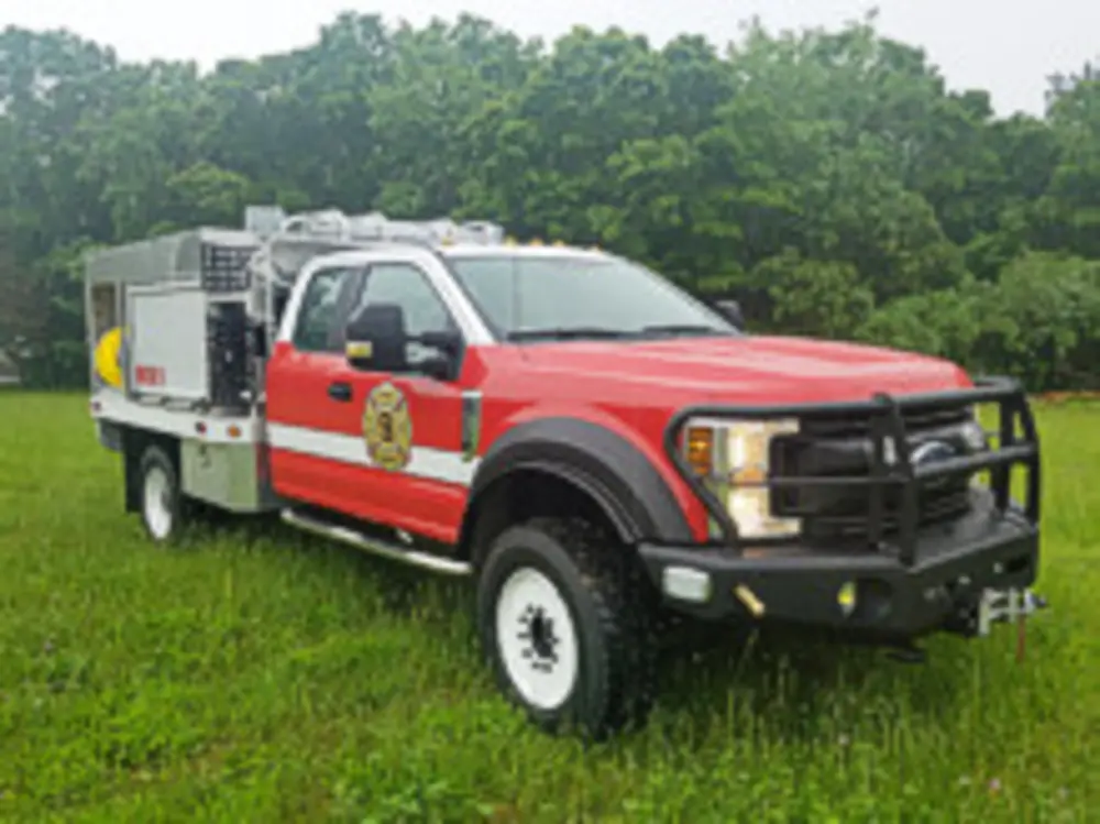 Exterior view of small fire truck showing cab, body compartments, and wheel/tire area.