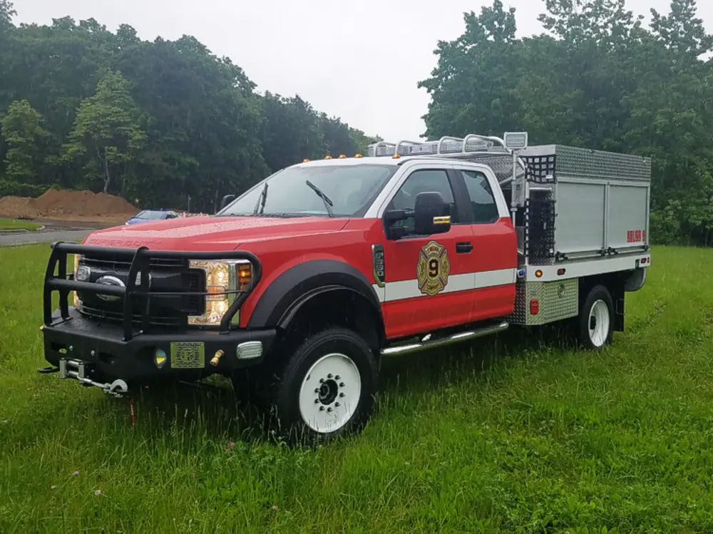 Exterior view of small fire truck showing cab, body compartments, and wheel/tire area.