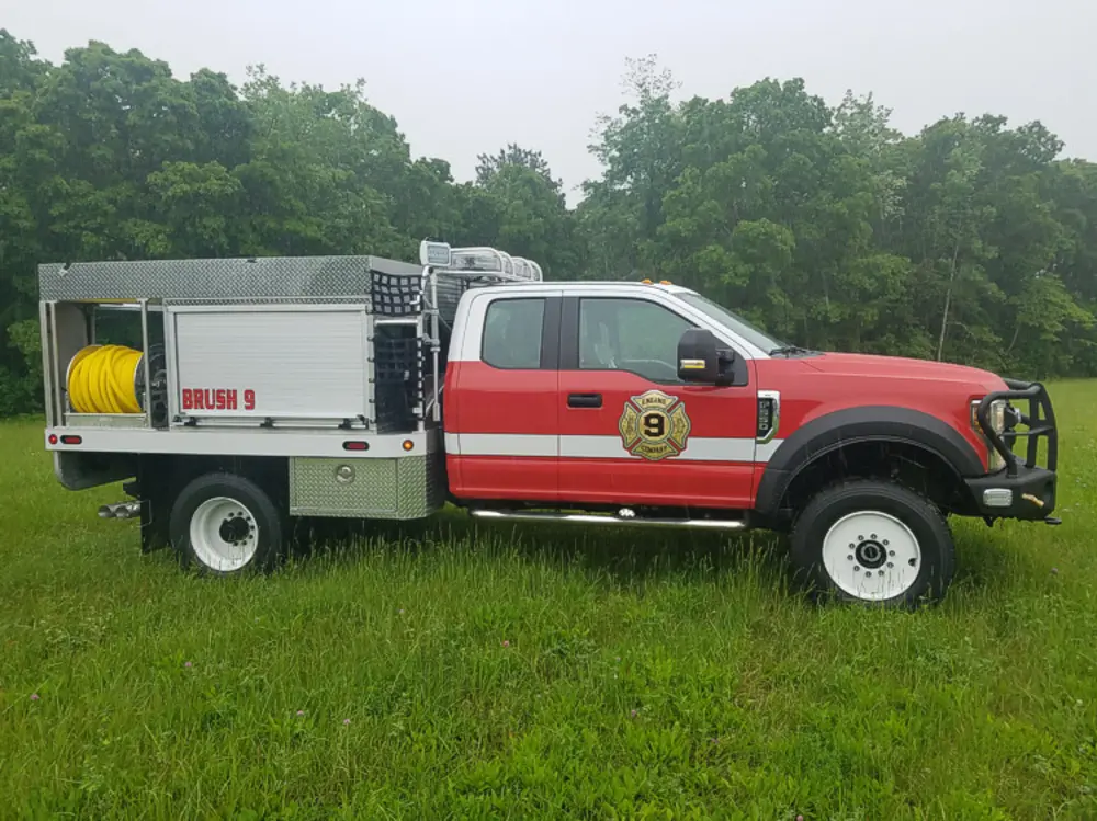 Exterior view of small fire truck showing cab, body compartments, and wheel/tire area.