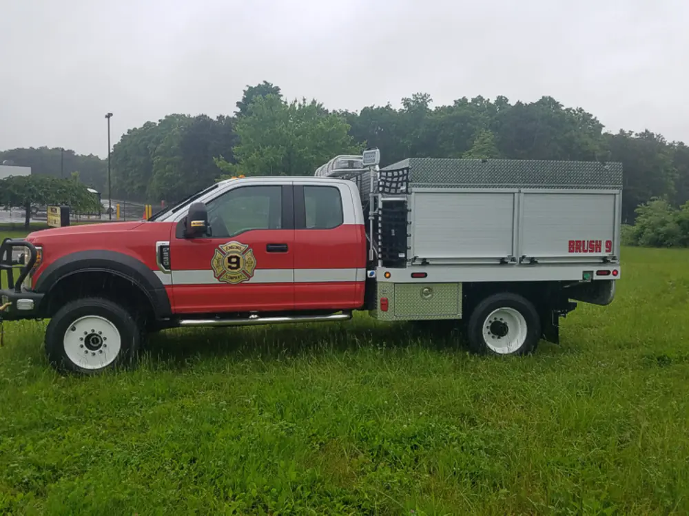 Exterior view of small fire truck showing cab, body compartments, and wheel/tire area.
