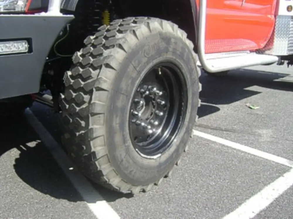 Exterior view of small fire truck showing cab, body compartments, and wheel/tire area.