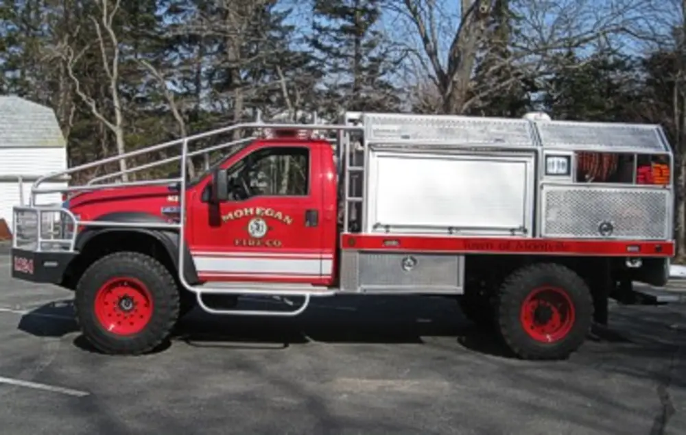 Exterior view of small fire truck showing cab, body compartments, and wheel/tire area.
