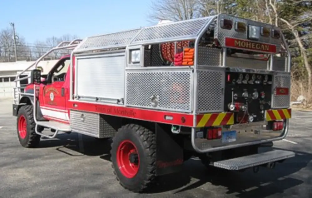 Exterior view of small fire truck showing cab, body compartments, and wheel/tire area.