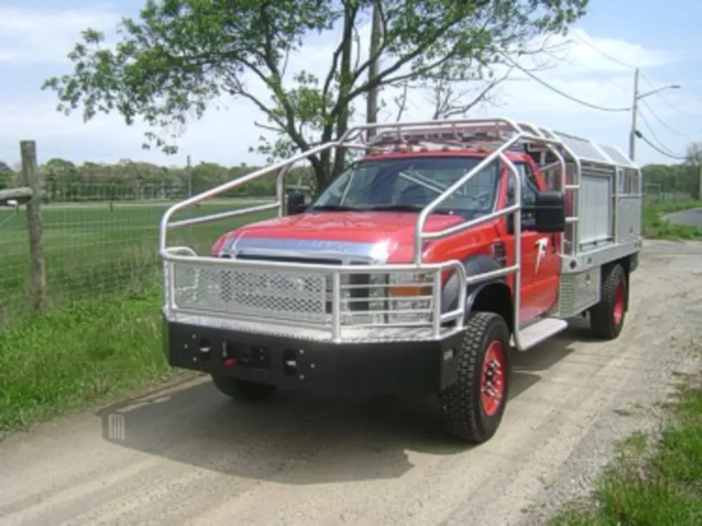 Exterior view of small fire truck showing cab, body compartments, and wheel/tire area.