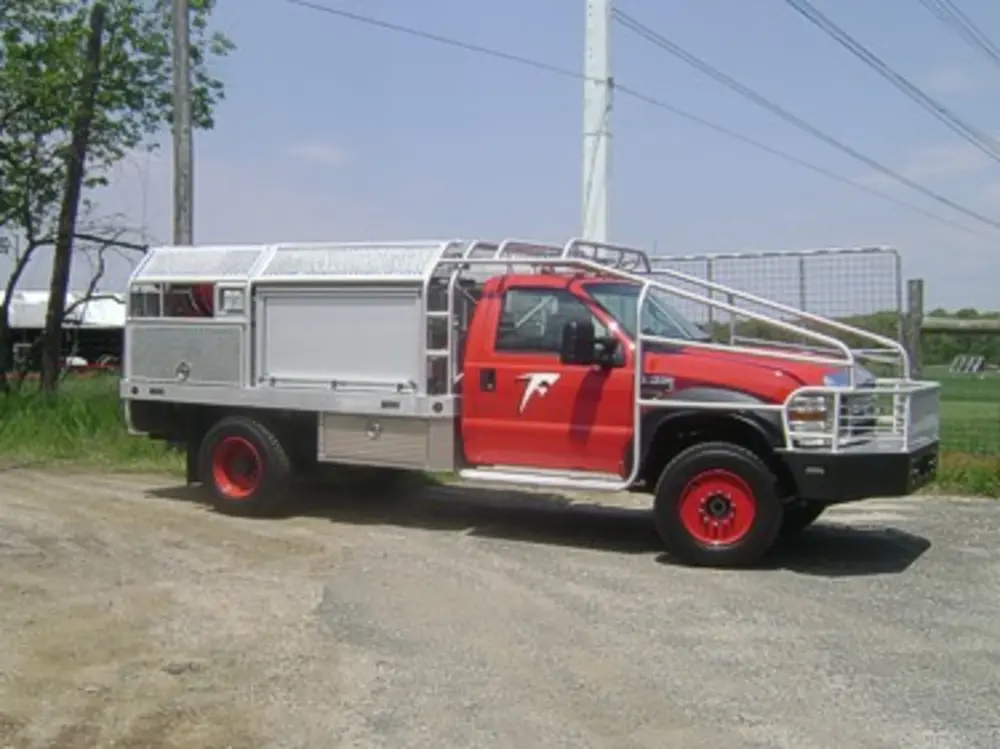 Exterior view of small fire truck showing cab, body compartments, and wheel/tire area.