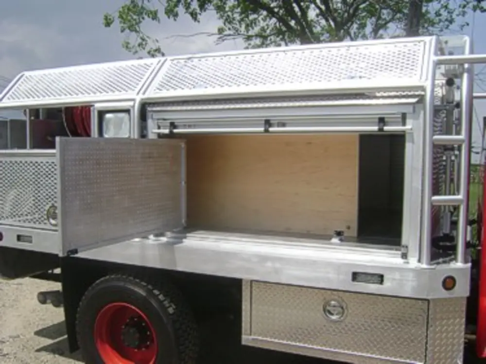Exterior view of small fire truck showing cab, body compartments, and wheel/tire area.