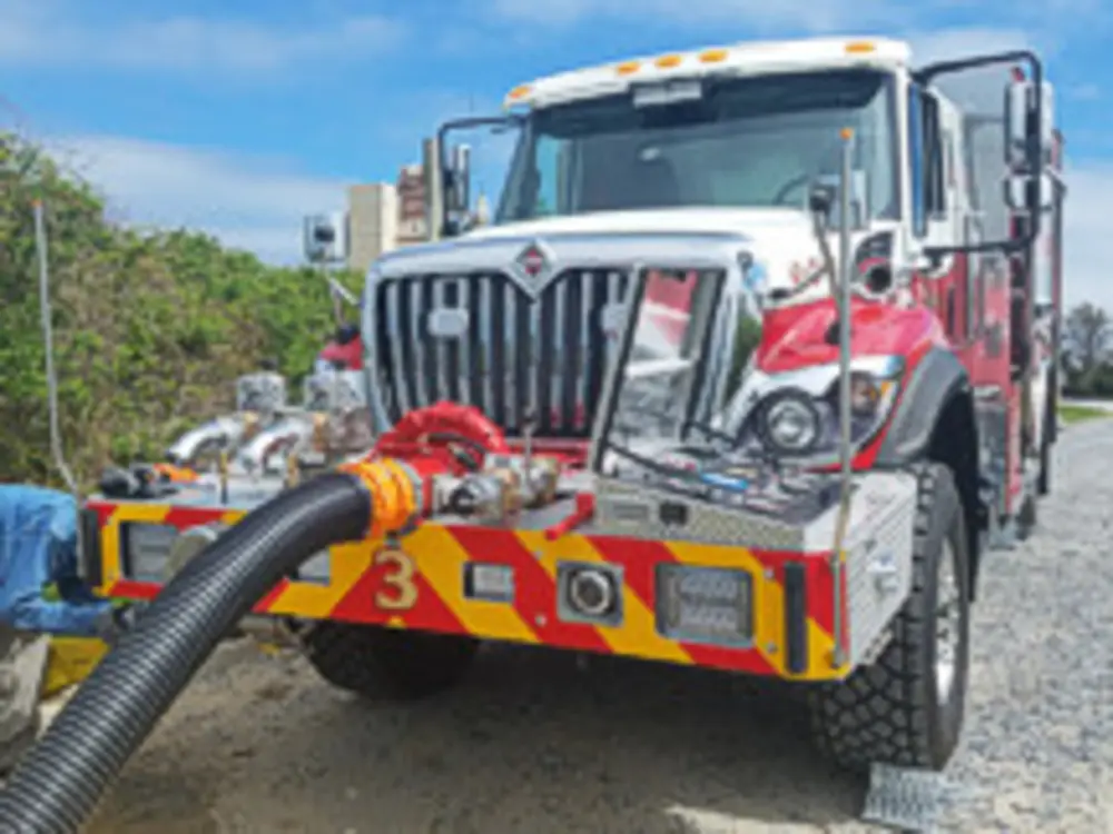 Exterior view of small fire truck showing cab, body compartments, and wheel/tire area.