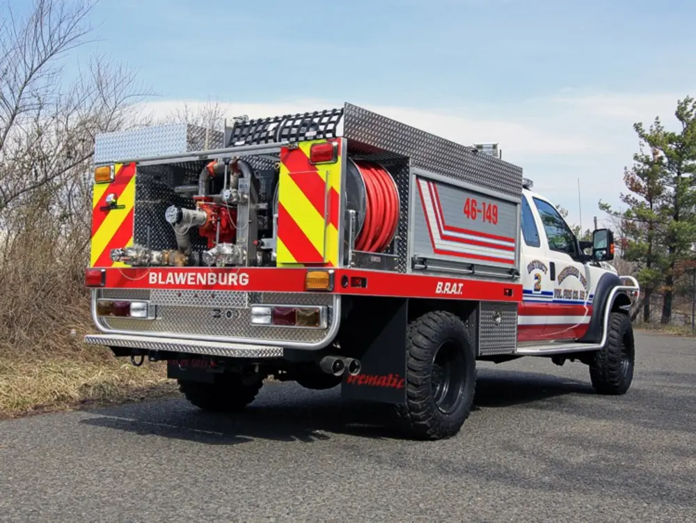Exterior view of small fire truck showing cab, body compartments, and wheel/tire area.