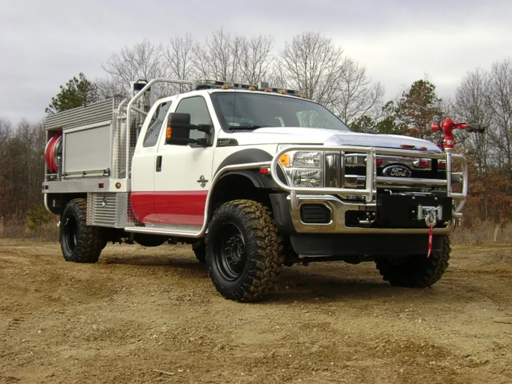Exterior view of small fire truck showing cab, body compartments, and wheel/tire area.