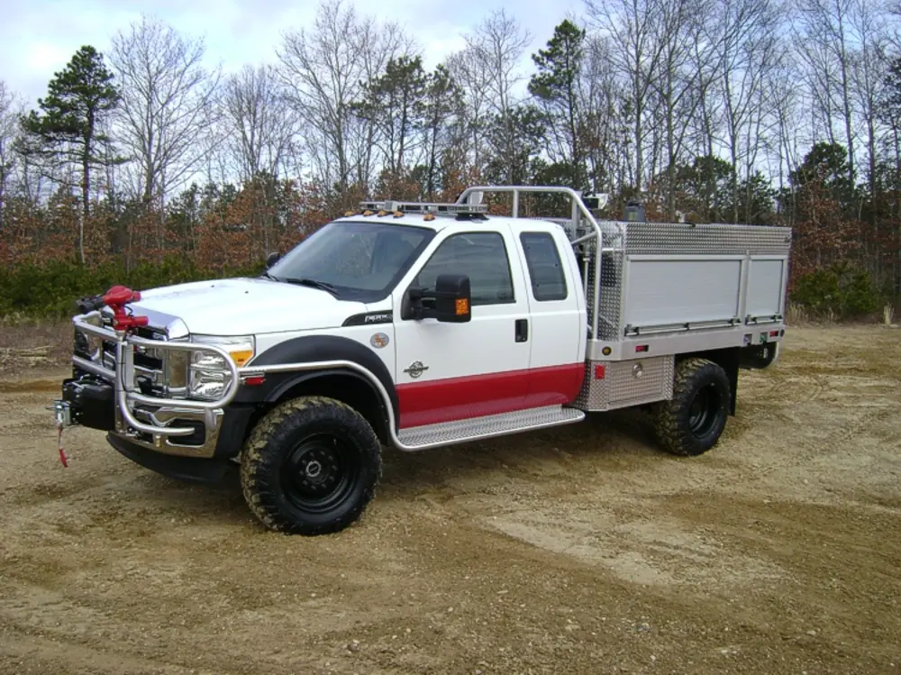 Exterior view of small fire truck showing cab, body compartments, and wheel/tire area.