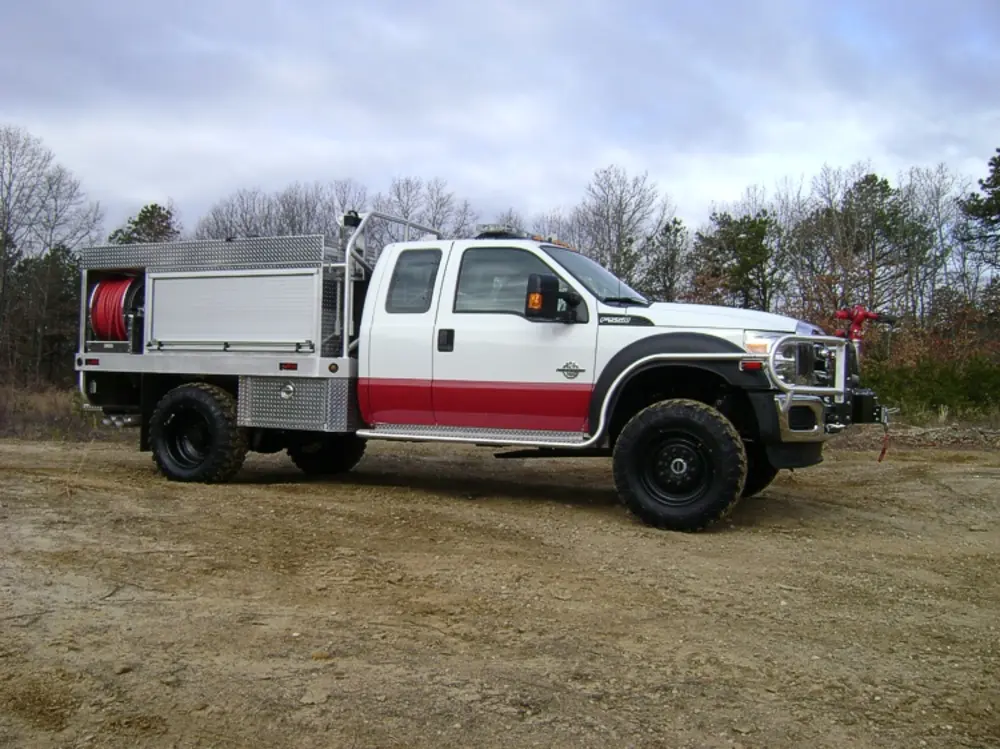 Exterior view of small fire truck showing cab, body compartments, and wheel/tire area.