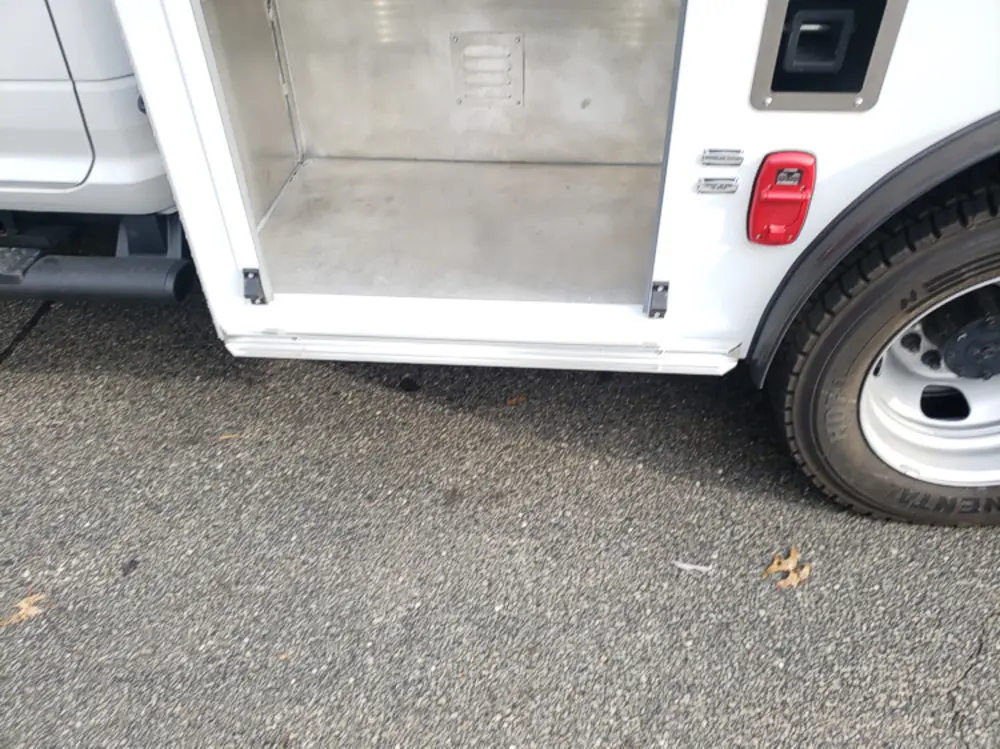 Exterior view of small fire truck showing cab, body compartments, and wheel/tire area.