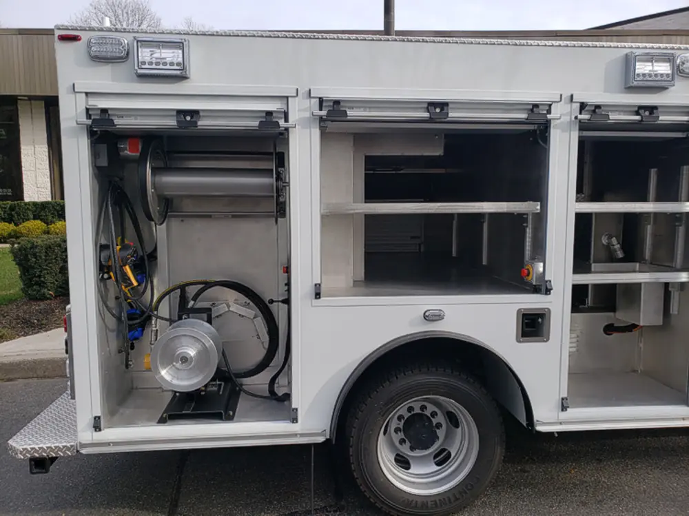 Exterior view of small fire truck showing cab, body compartments, and wheel/tire area.
