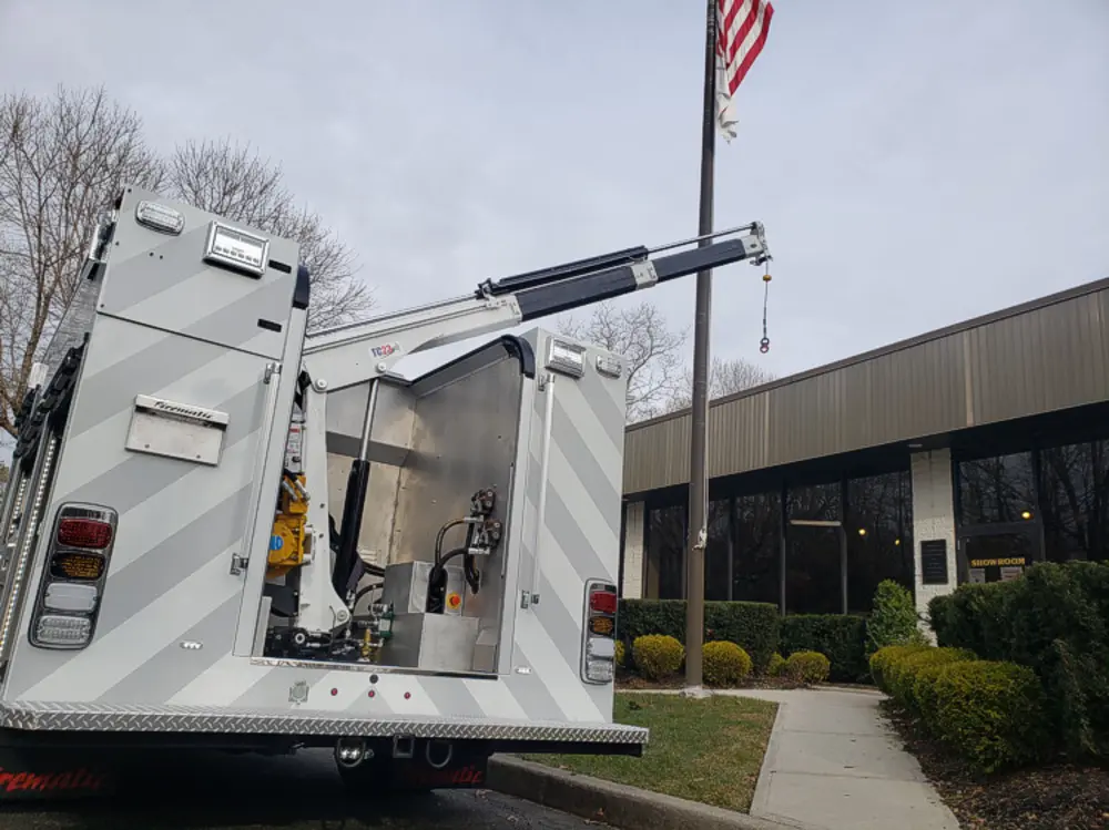 Exterior view of small fire truck showing cab, body compartments, and wheel/tire area.
