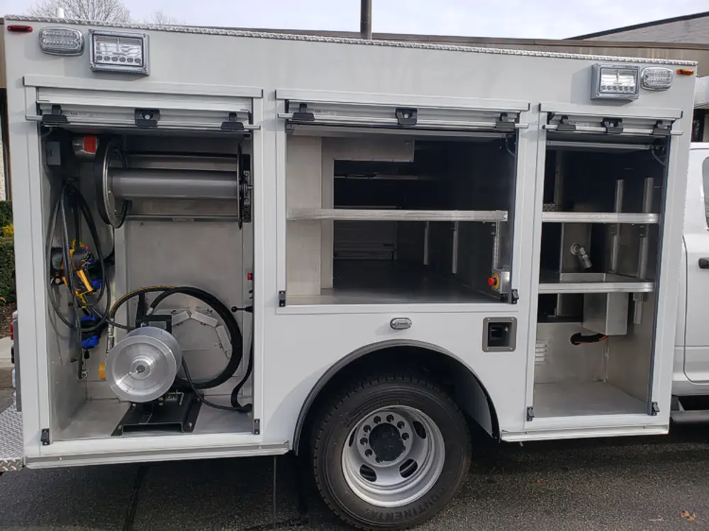 Exterior view of small fire truck showing cab, body compartments, and wheel/tire area.