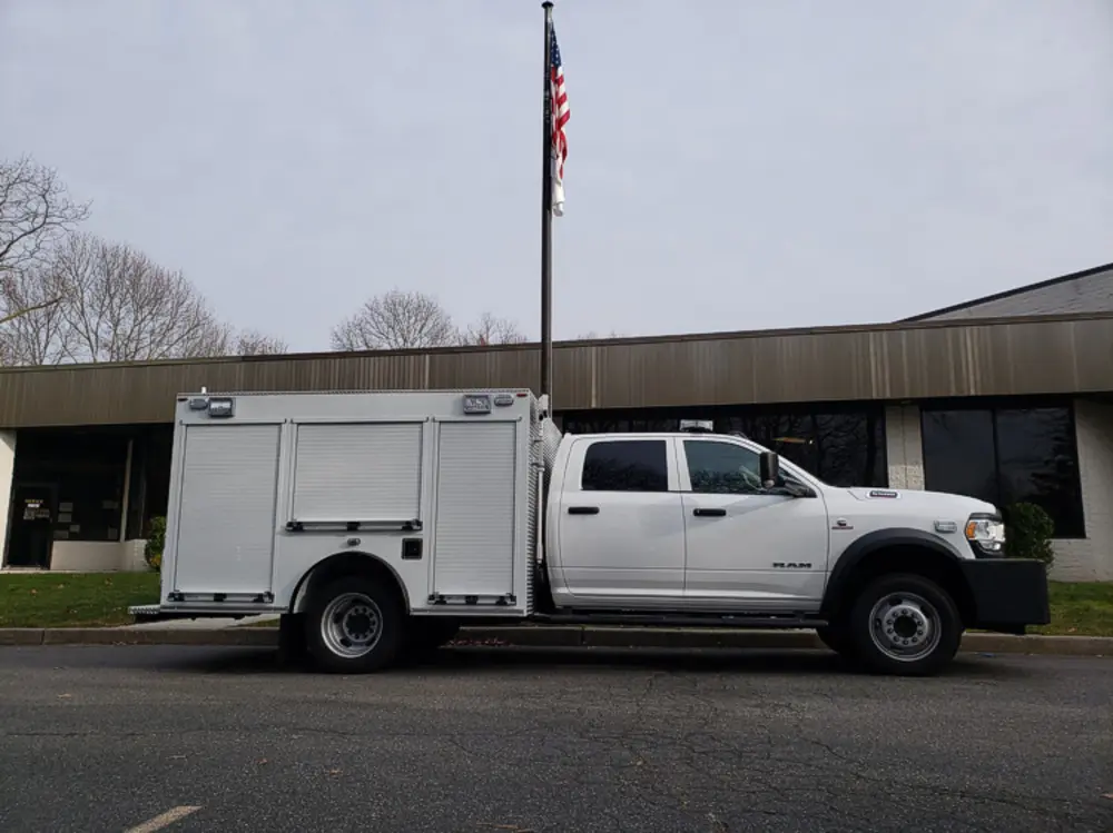 Exterior view of small fire truck showing cab, body compartments, and wheel/tire area.